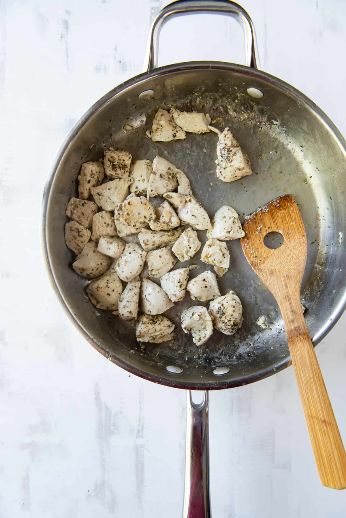 Pieces of chicken cook in a skillet with a wooden spoon.