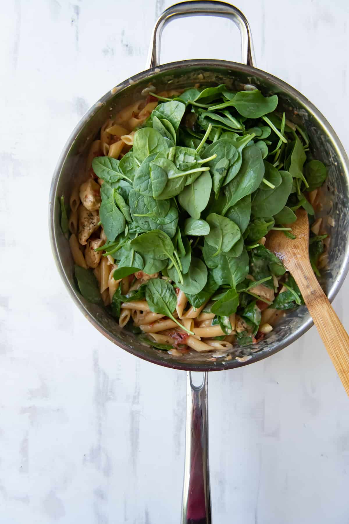 Baby spinach piled on top of pasta in a skillet.