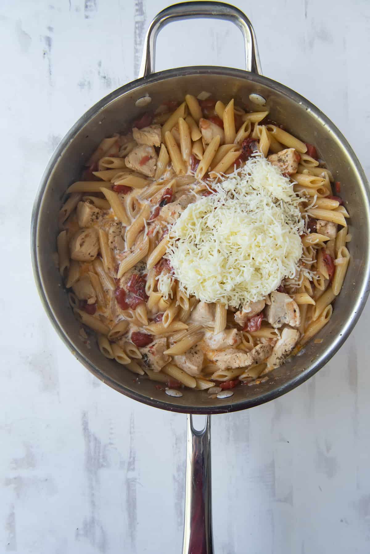 Cheese and cream added to cooked pasta in a skillet.