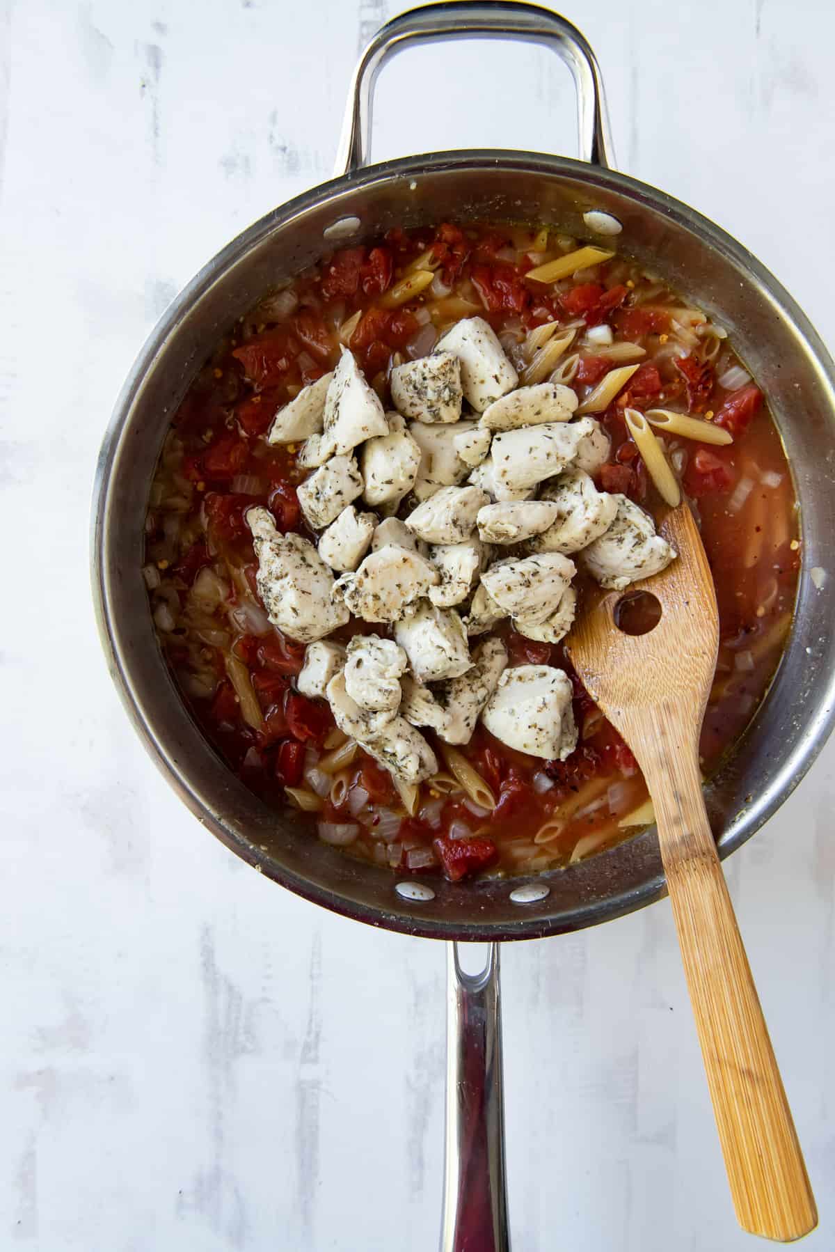 Cooked chicken added to pasta and tomatoes in a skillet.