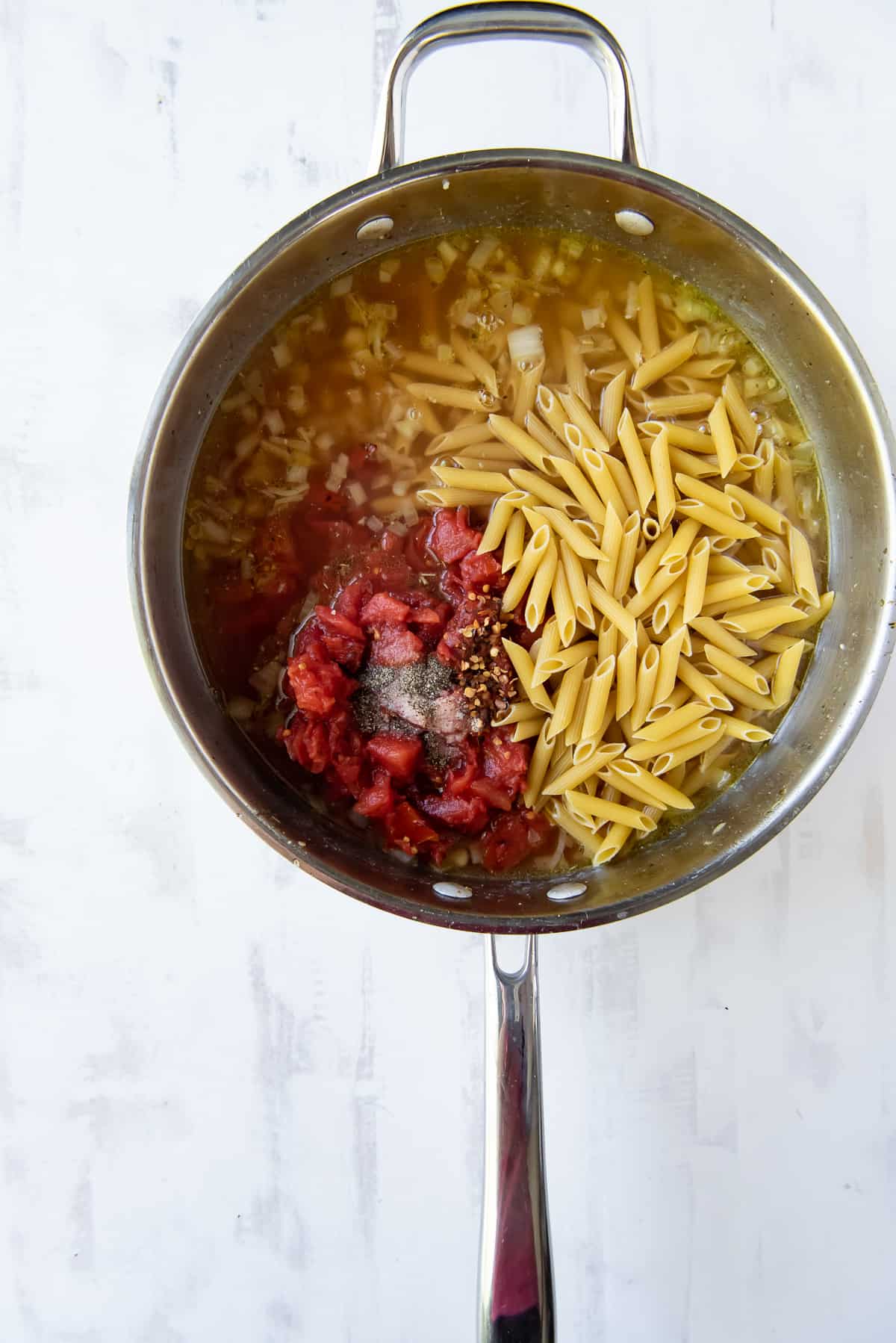 Pasta, broth, and tomatoes in a skillet.