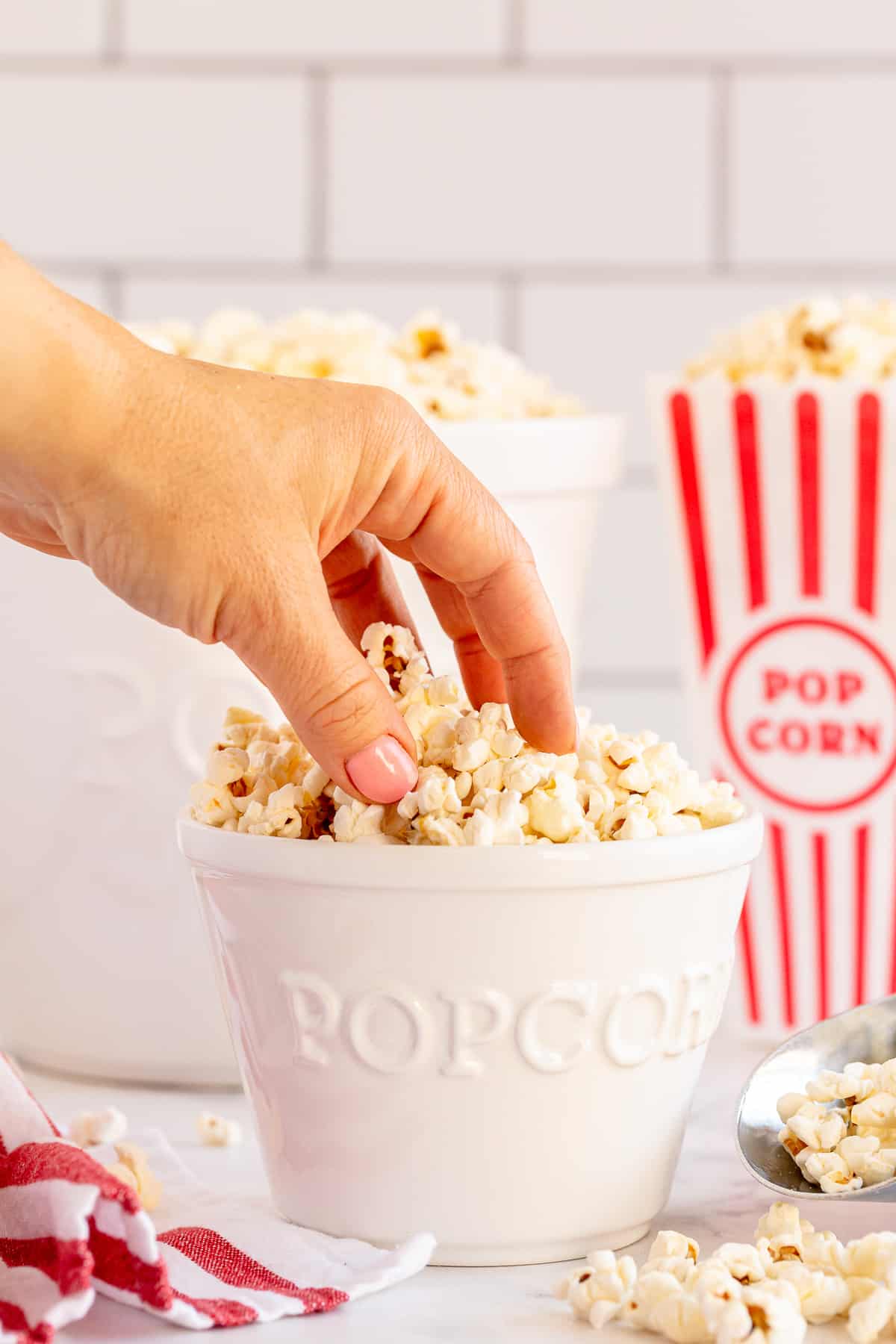 A hand reaches for popcorn from a white popcorn bowl.