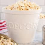 A metal scoop and a tall white bowl filled with popcorn.