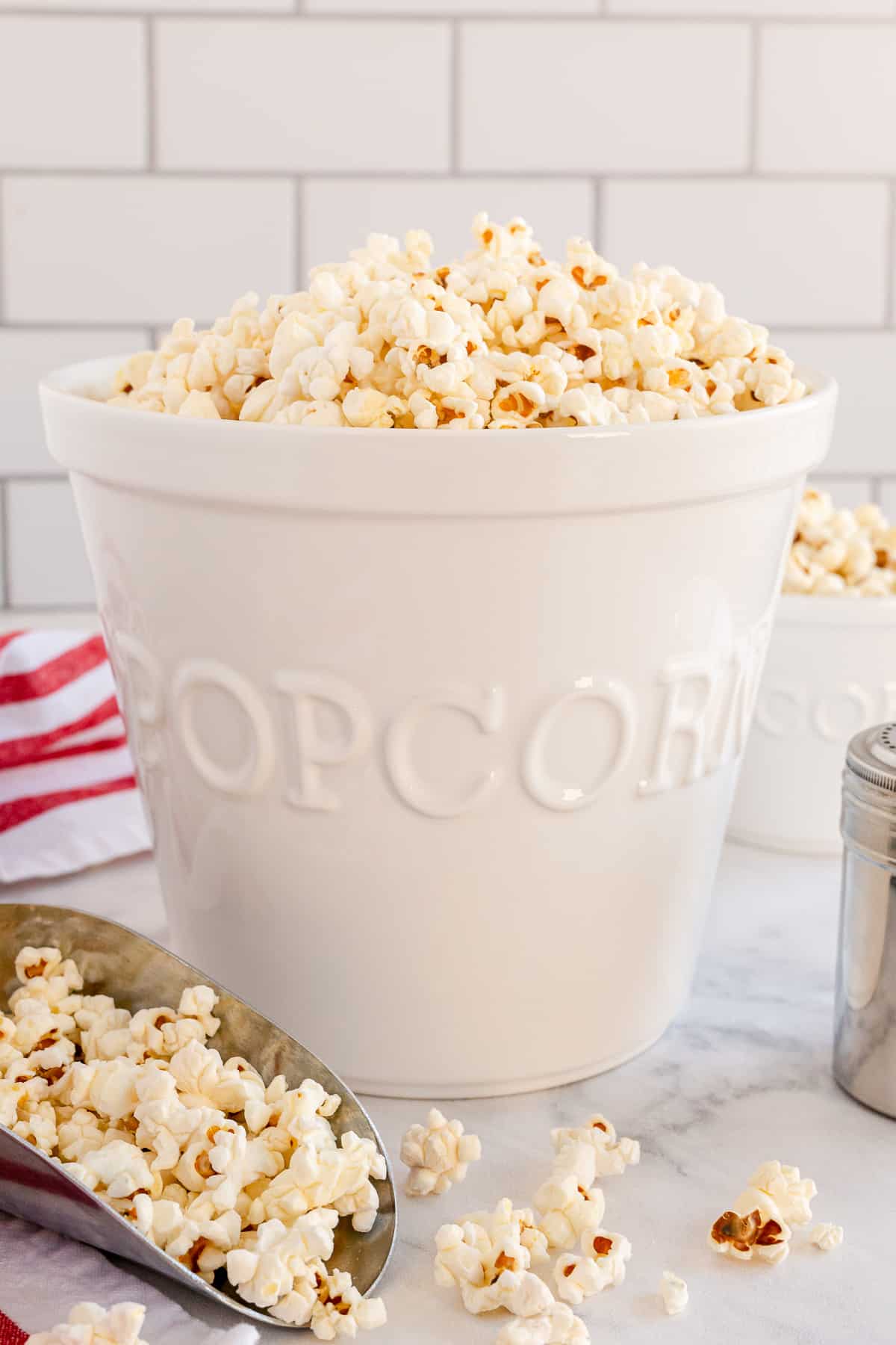 A metal scoop and a tall white bowl filled with popcorn.