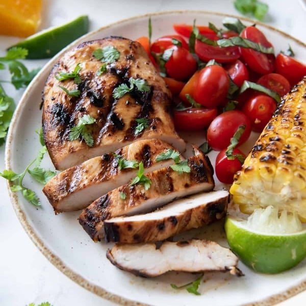Sliced grilled chicken on a plate with cherry tomatoes and corn.