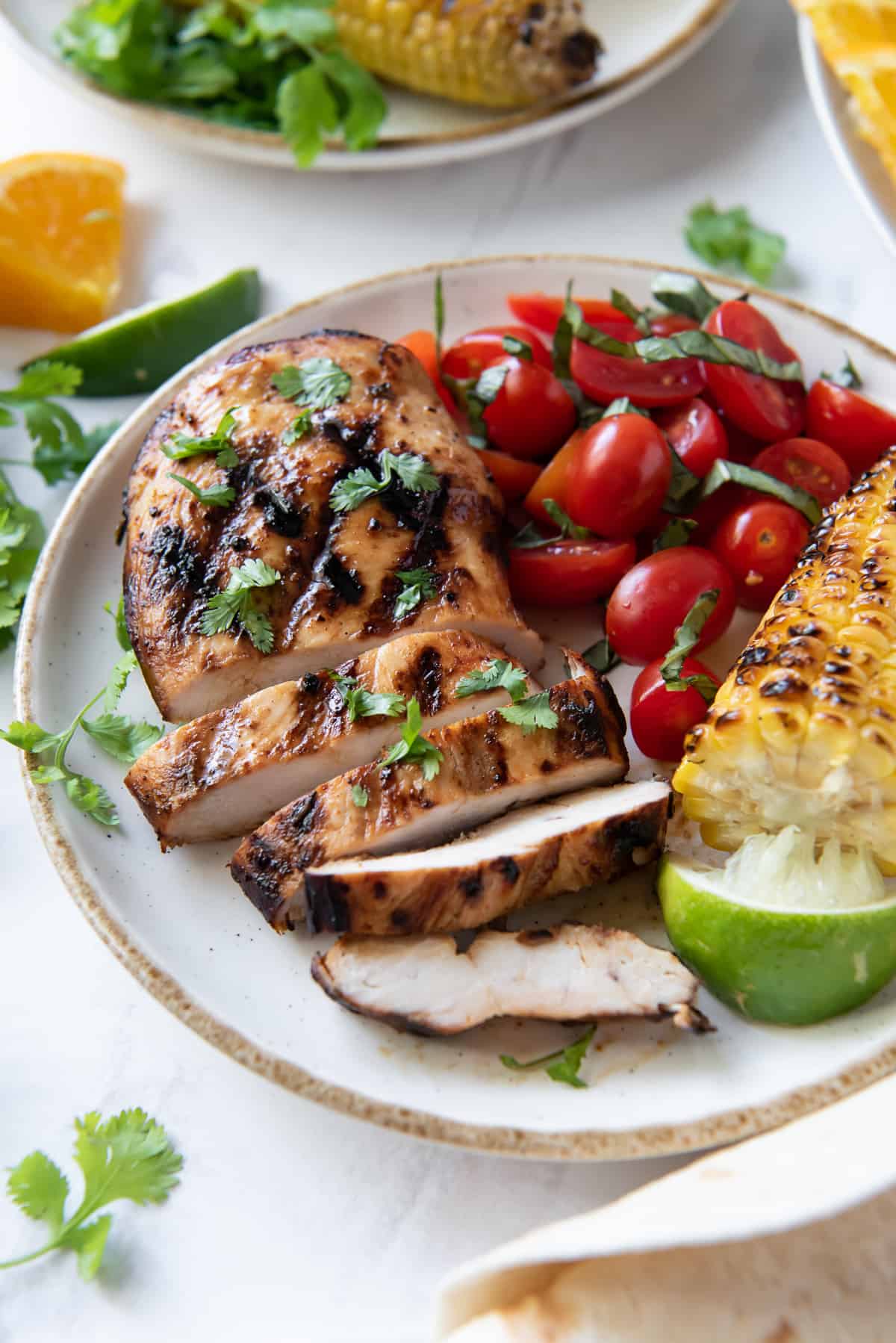 Sliced grilled chicken on a plate with cherry tomatoes and corn.