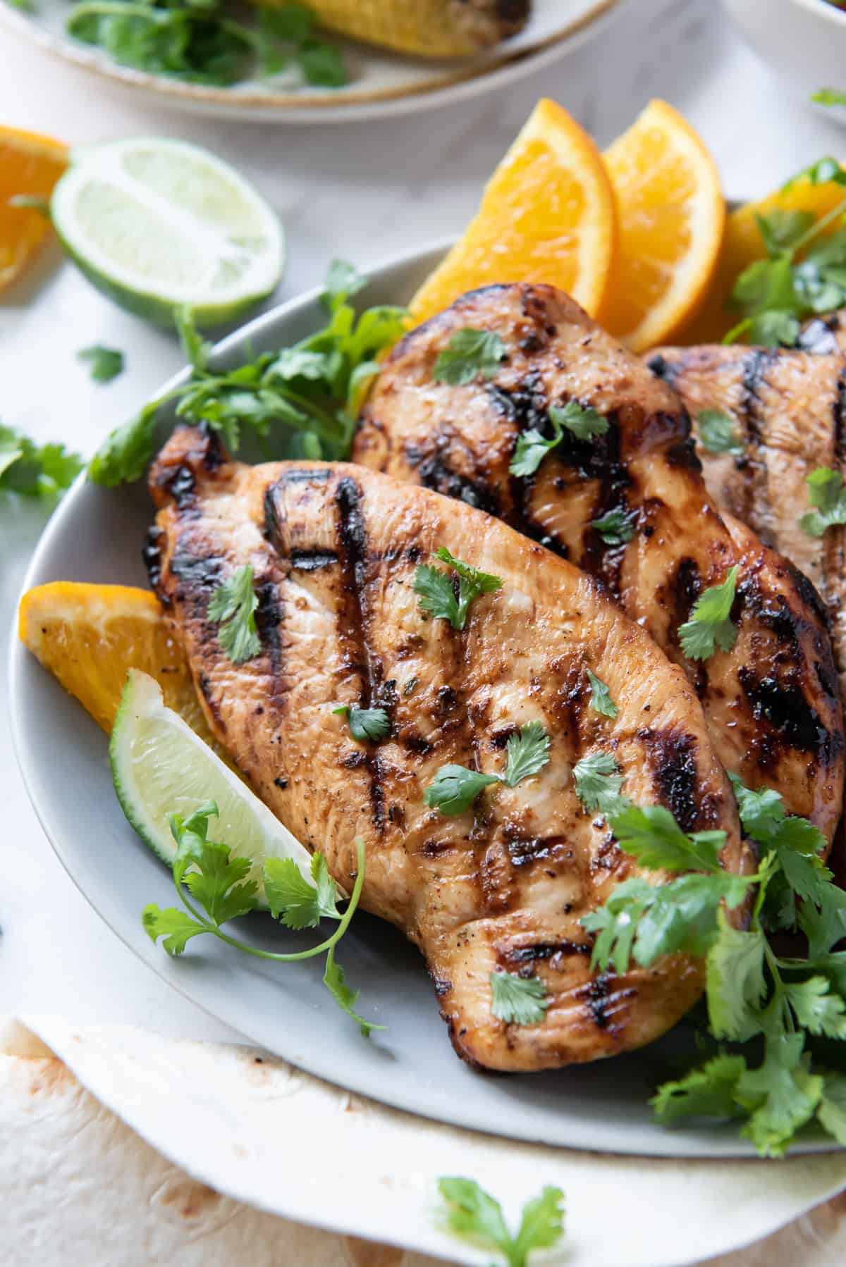 Grilled chicken on a plate with cilantro and orange slices.