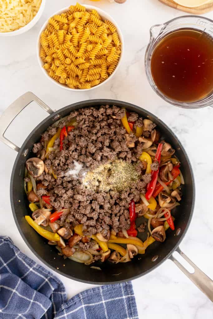 Cooked ground beef and seasoning in a skillet with onion and peppers.