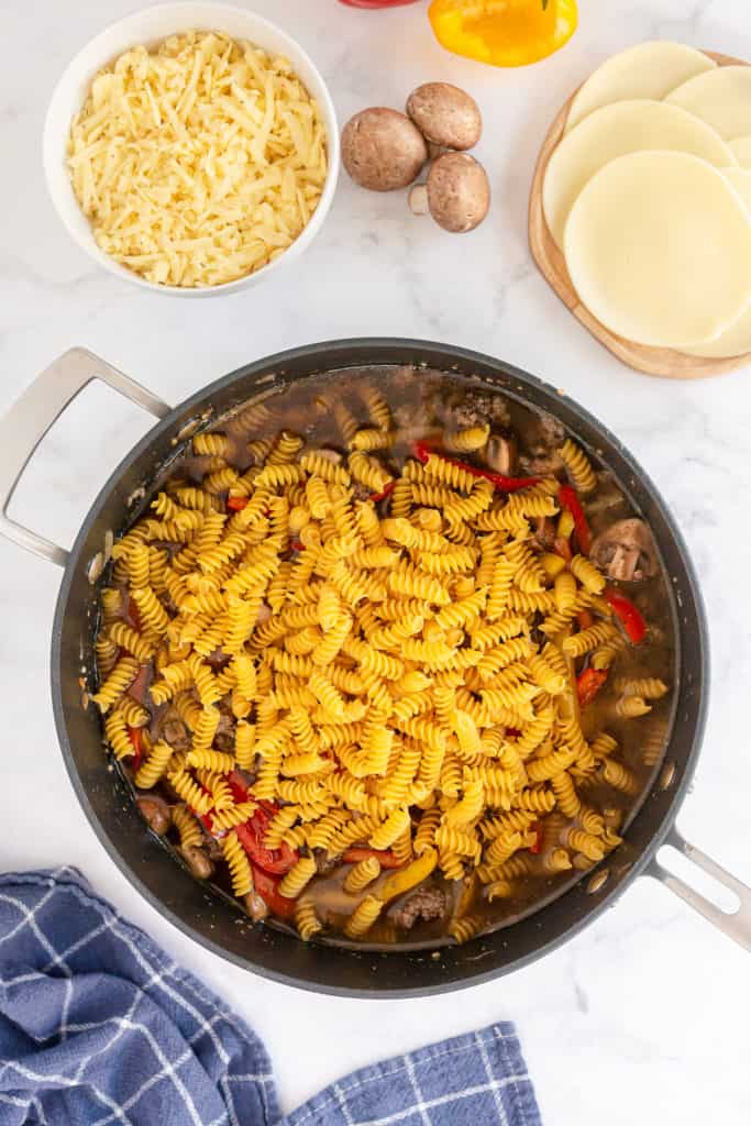 Uncooked dry pasta is added to a skillet with other ingredients.
