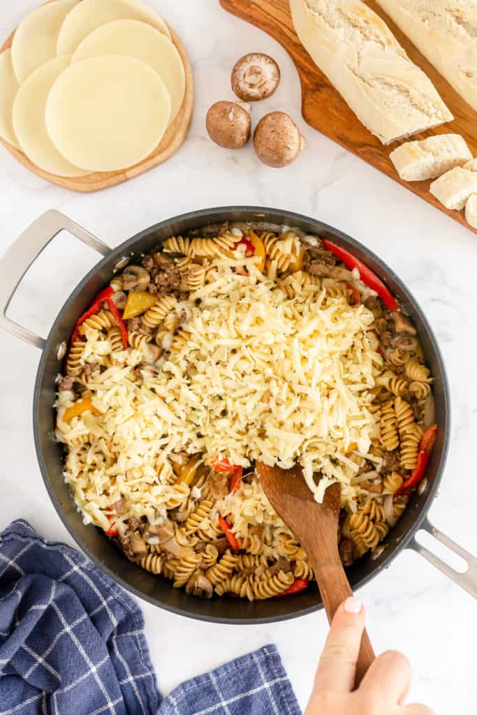 Shredded mozzarella is added to a skillet of pasta.