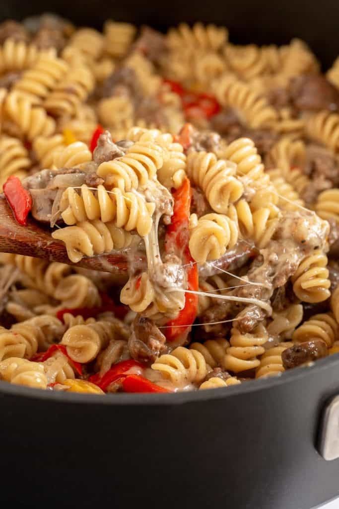 A spoon scoops fusilli pasta from a skillet.