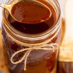 A spoon scoops bbq sauce from a mason jar.