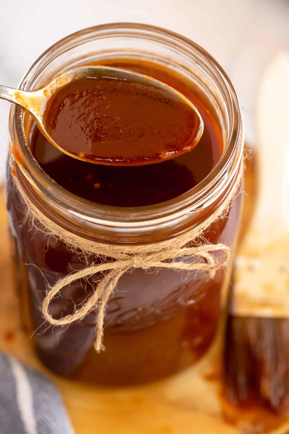 A spoon scoops bbq sauce from a mason jar.