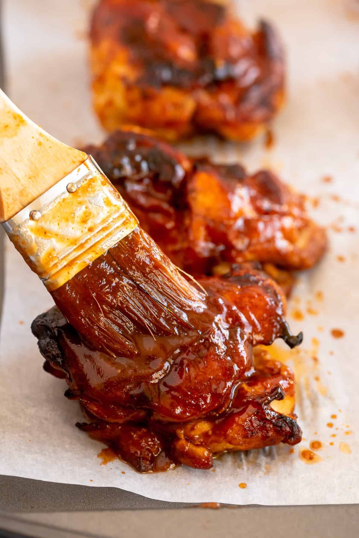 A pastry brush bastes grilled chicken with BBQ sauce.