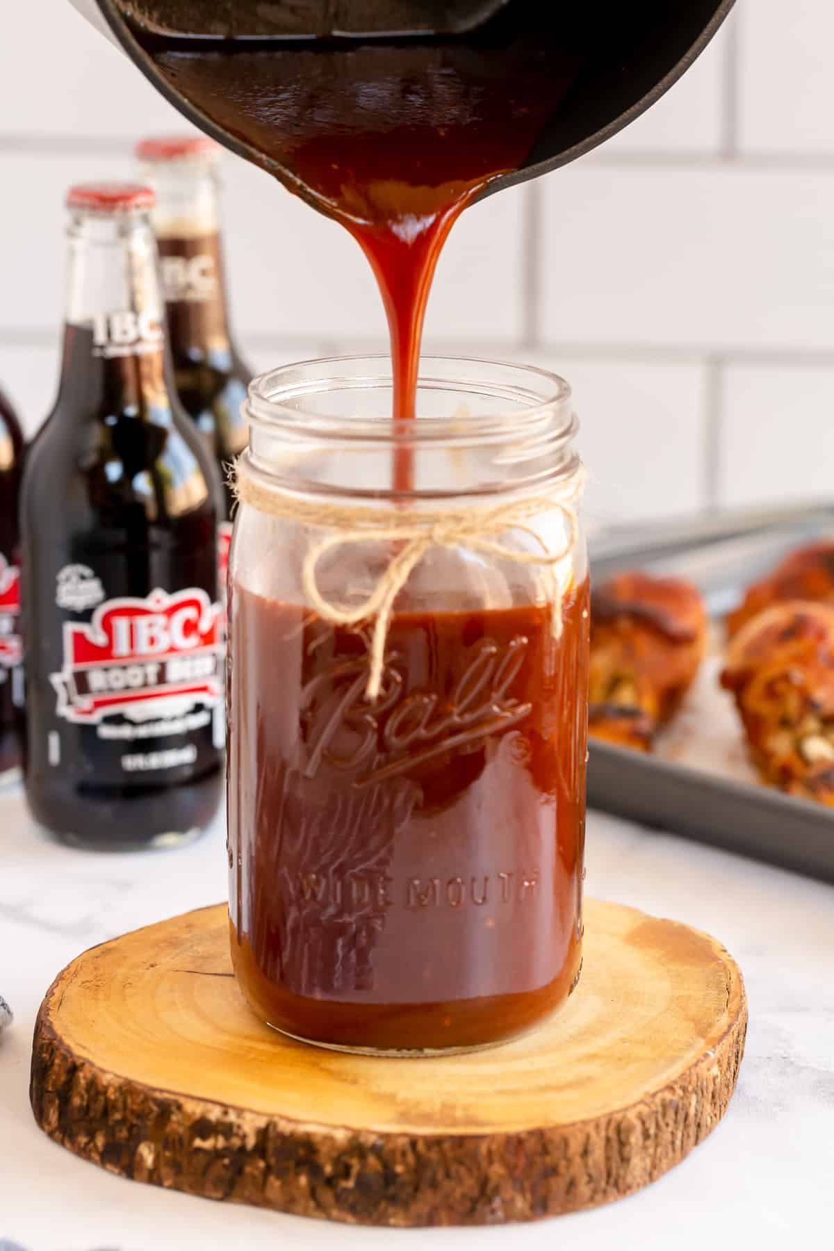 Root Beer BBQ Sauce is poured from a pot into a mason jar.