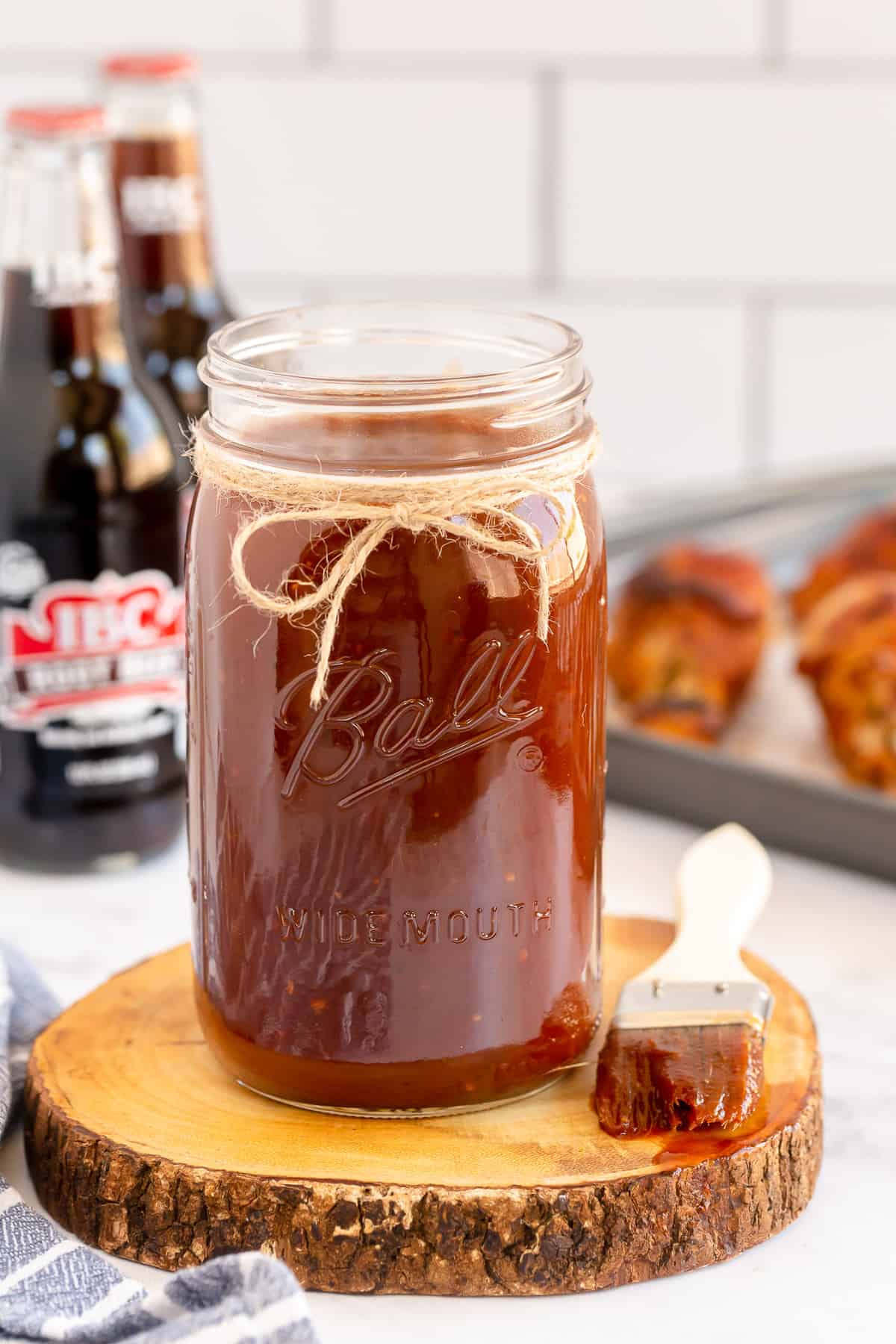 A pastry brush rests next to a mason jar filled with BBQ sauce.