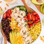 A salad with chicken, avocado, black beans, corn, and tomatoes shot from over the top.