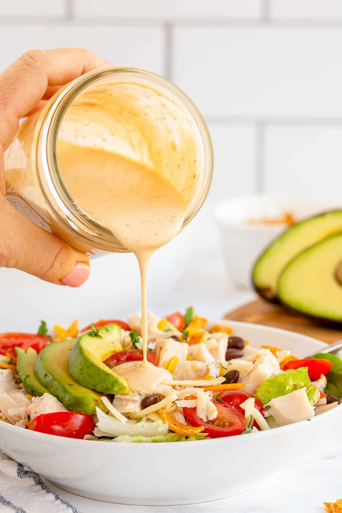 Southwest Caesar salad dressing is poured from a mason jar on to a salad.