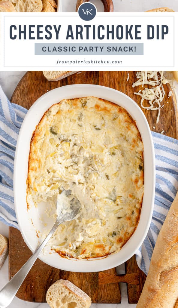 A spoon rests in a baking dish full of Artichoke Dip with text overlay.