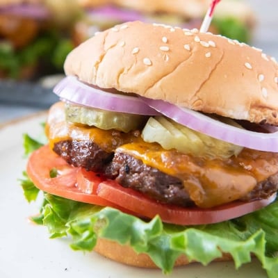 A closeup of a beef burger with cheese on a white plate.