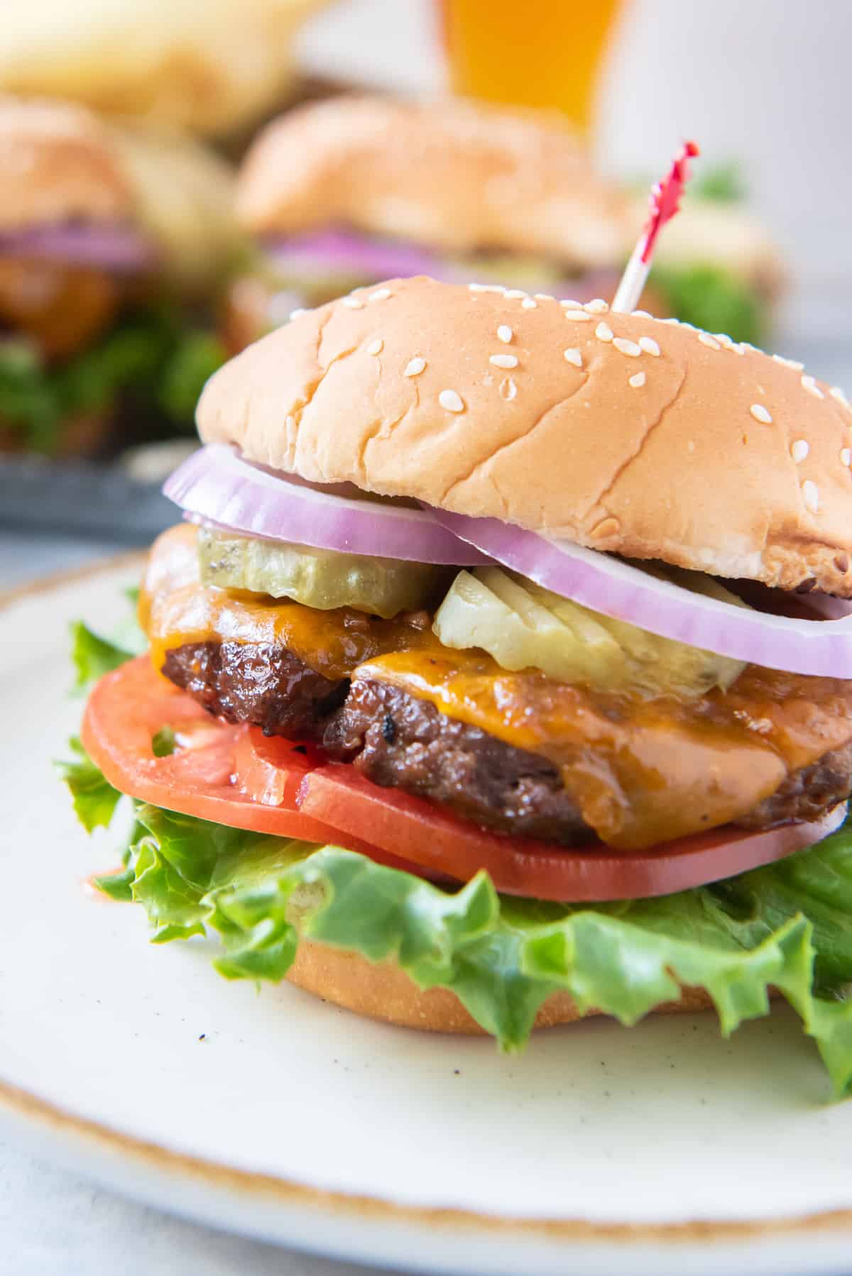 A closeup of a beef burger with cheese on a white plate.