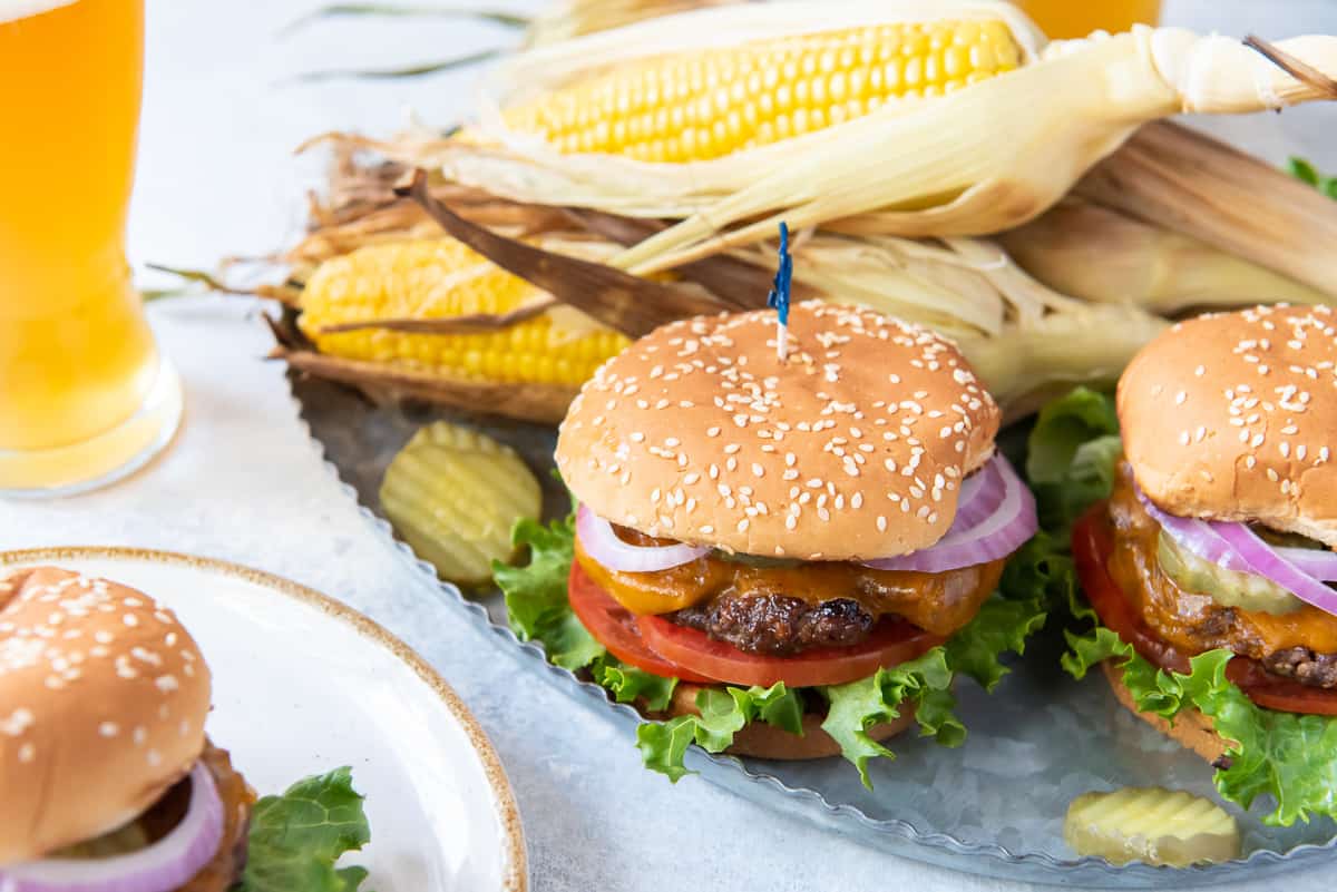 A cheeseburger on a metal platter with corn on the cob.
