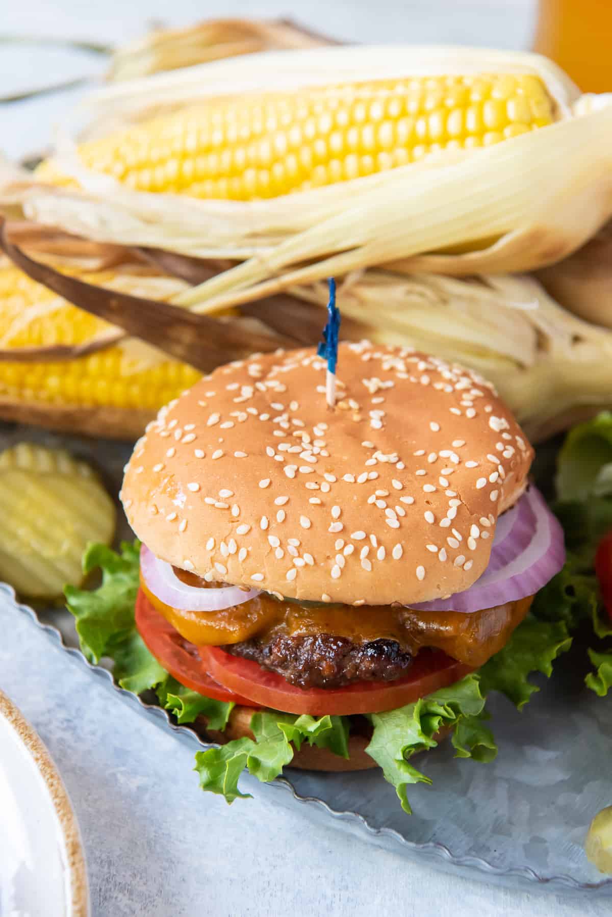 A burger on a silver platter with corn on the cob.
