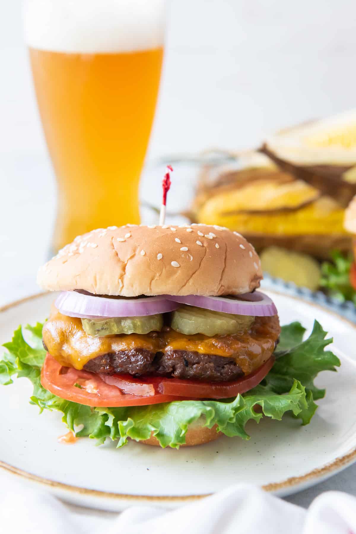A beef burger with cheese on a plate with a beer in the background.