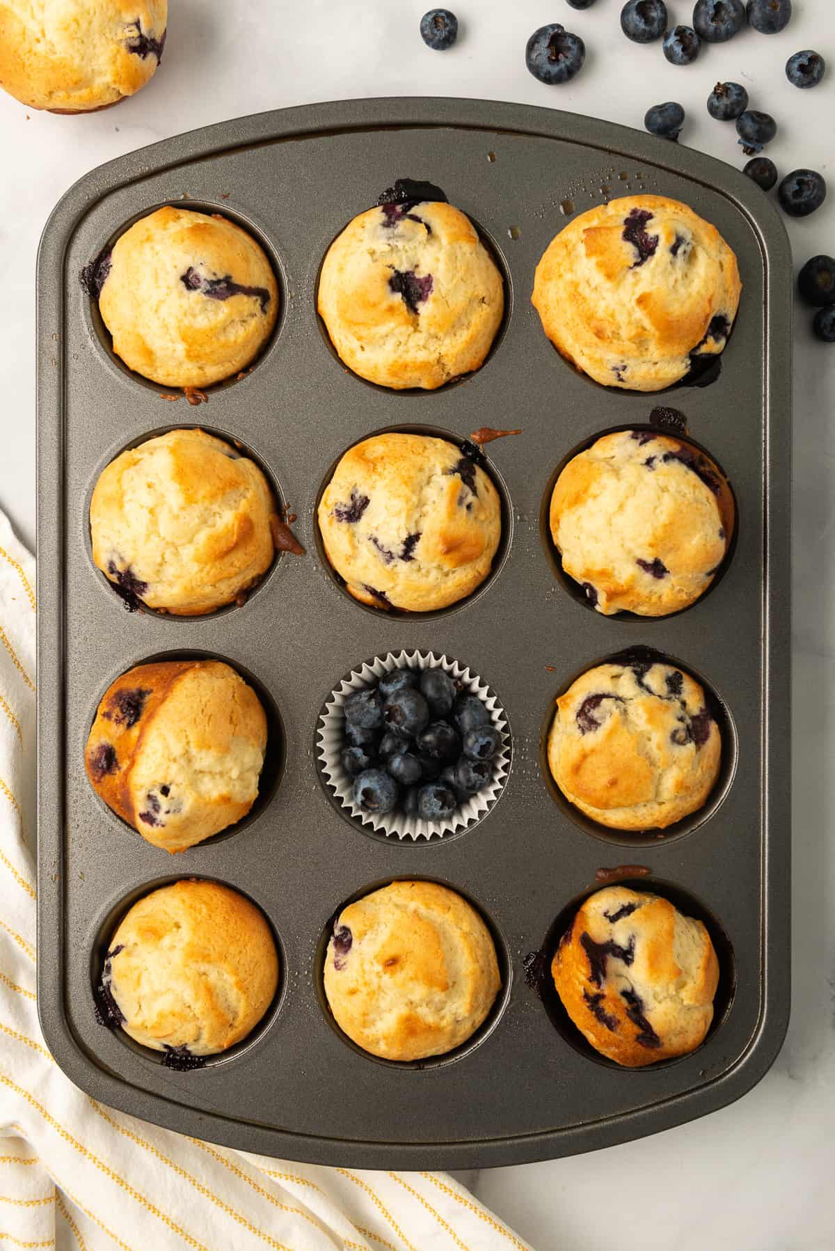 A muffin pan filled with blueberry muffins and fresh blueberries.