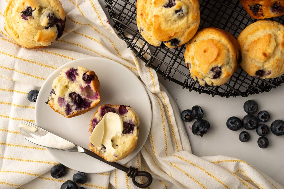 A blueberry muffin cut in half with butter on a plate.