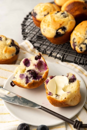 A blueberry muffin cut in half and topped with butter.