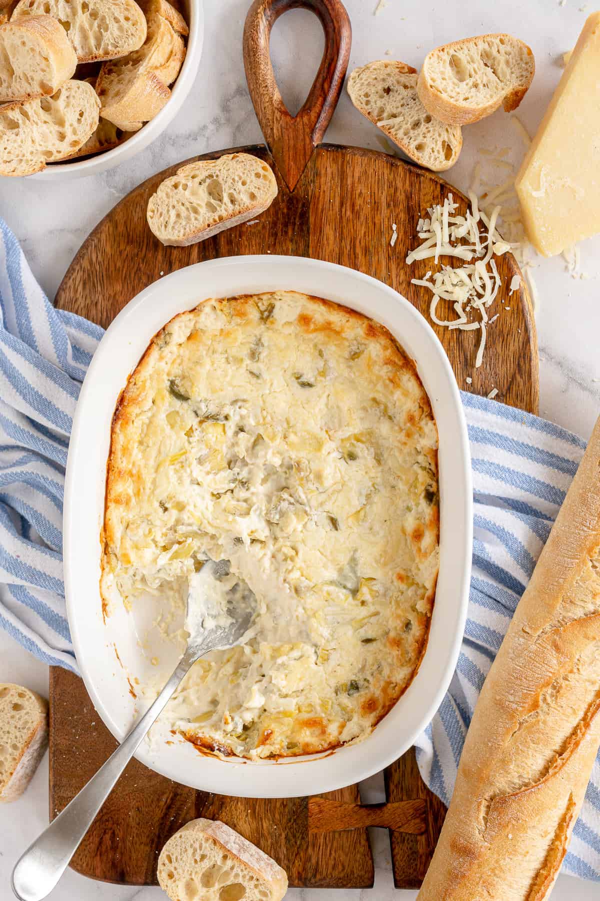 A spoon rests in a baking dish full warm dip.