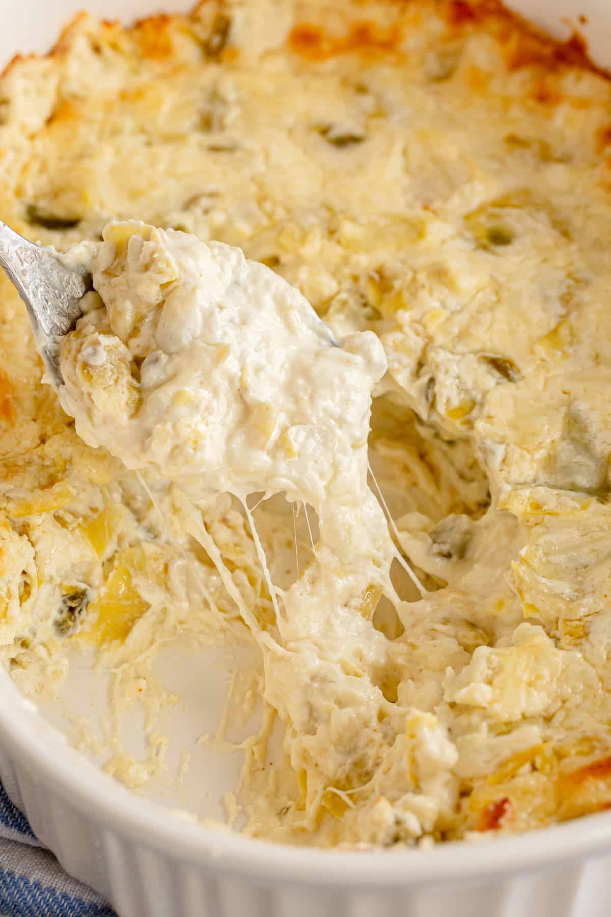 A spoon scoops cheesy dip from a baking dish.