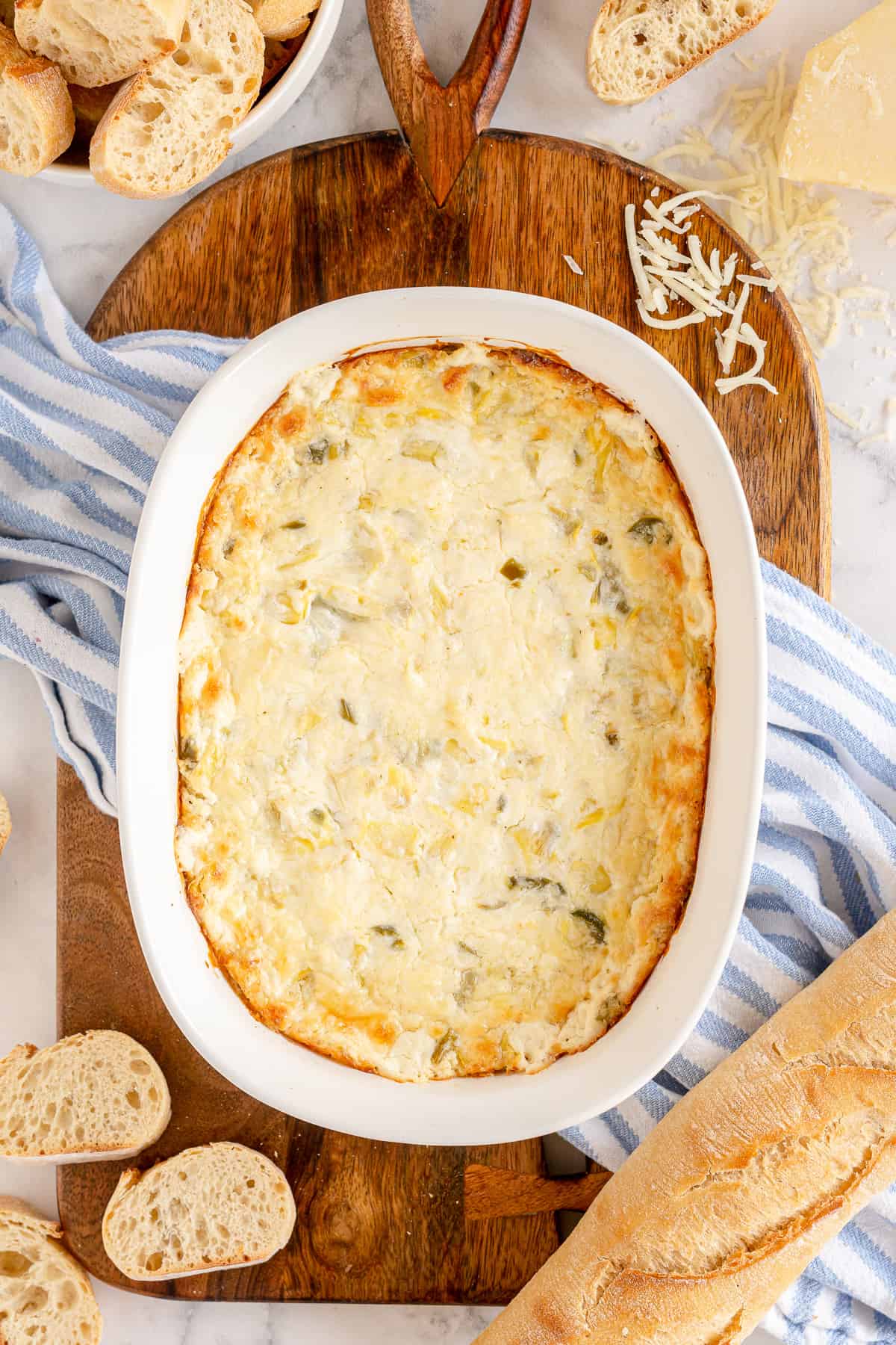 A baking dish full of dip on a cutting board with a baguette.