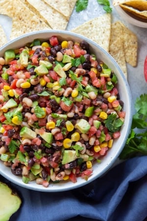 A bowl of Cowboy Caviar next to a blue cloth a tortilla chips.