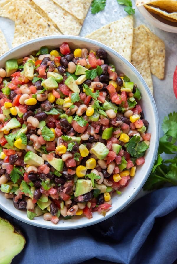 A bowl of Cowboy Caviar next to a blue cloth a tortilla chips.