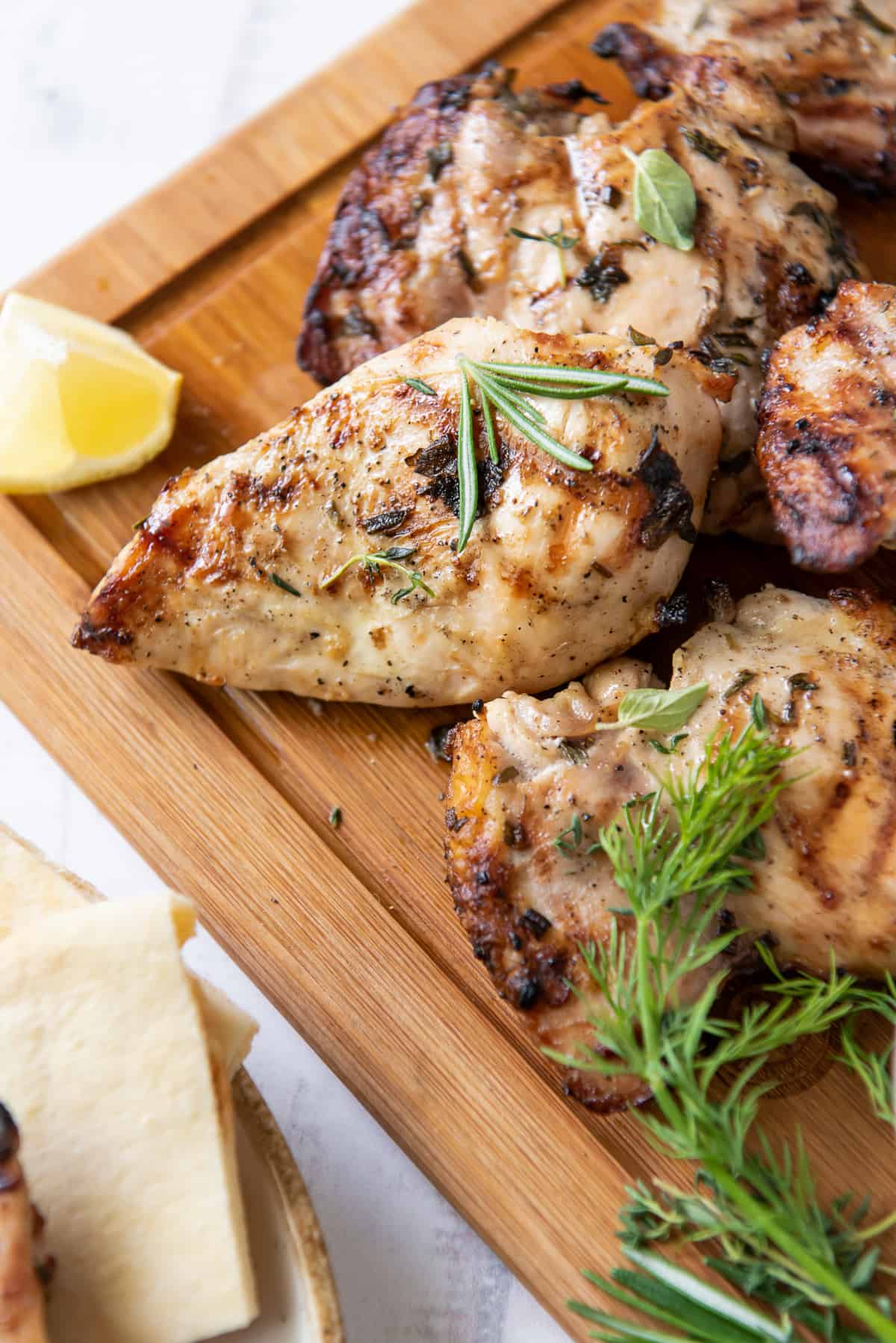 Grilled Greek Chicken on a cutting board with lemon wedges and fresh herbs.