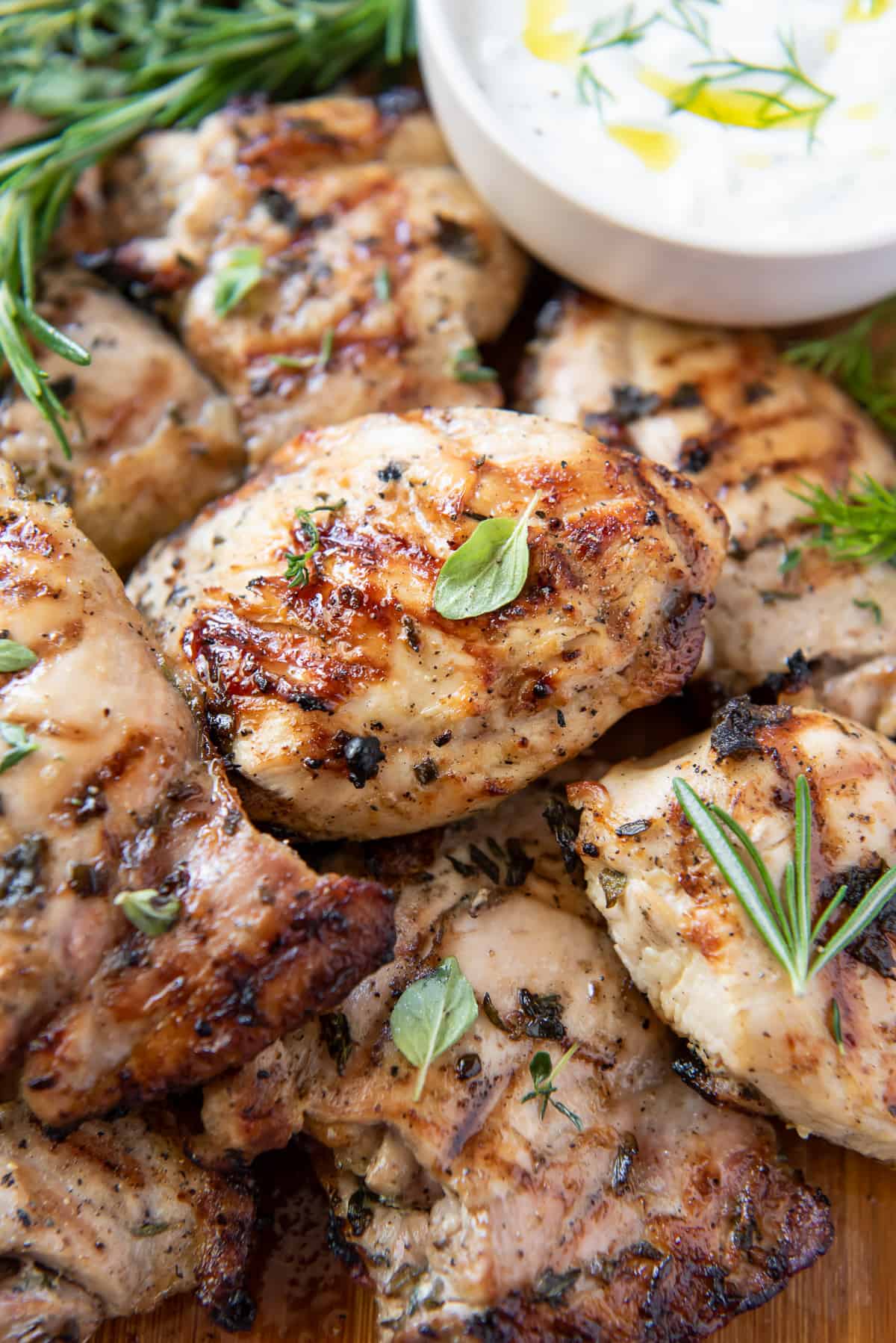 Grilled Greek Chicken topped with fresh herbs piled on a board.