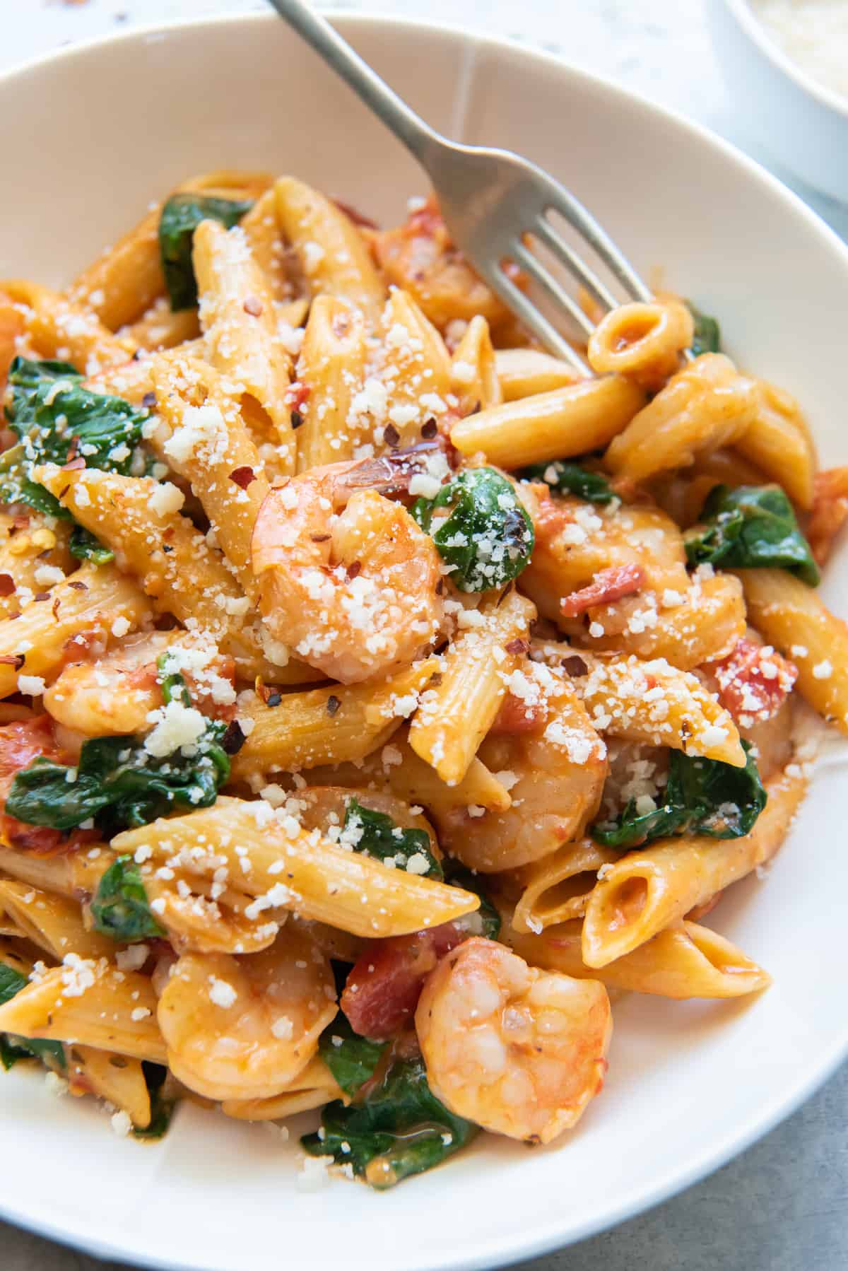 A close up of a bowl of shrimp and spinach pasta with a fork.