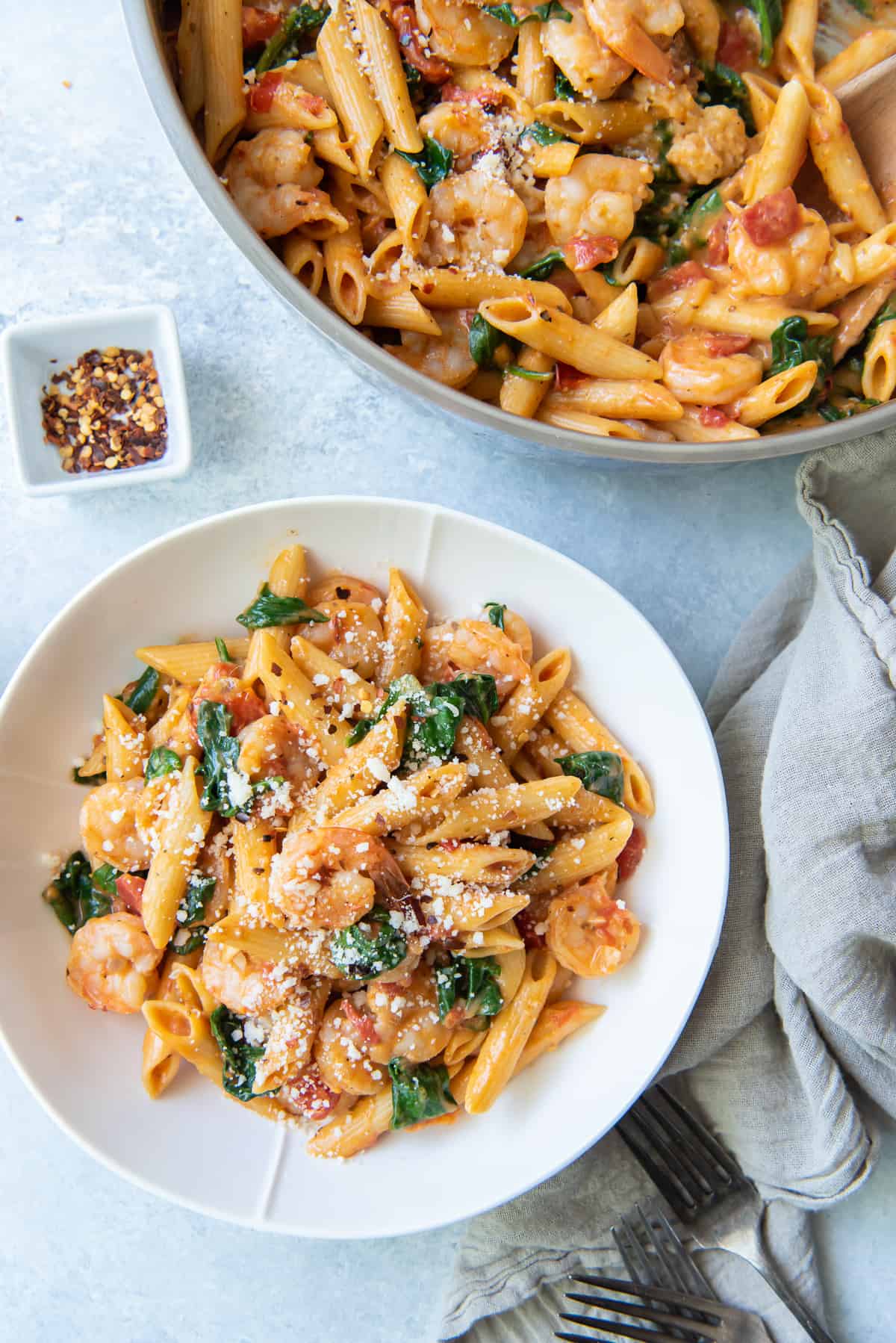 A skillet full of shrimp pasta next to a serving in a bowl.