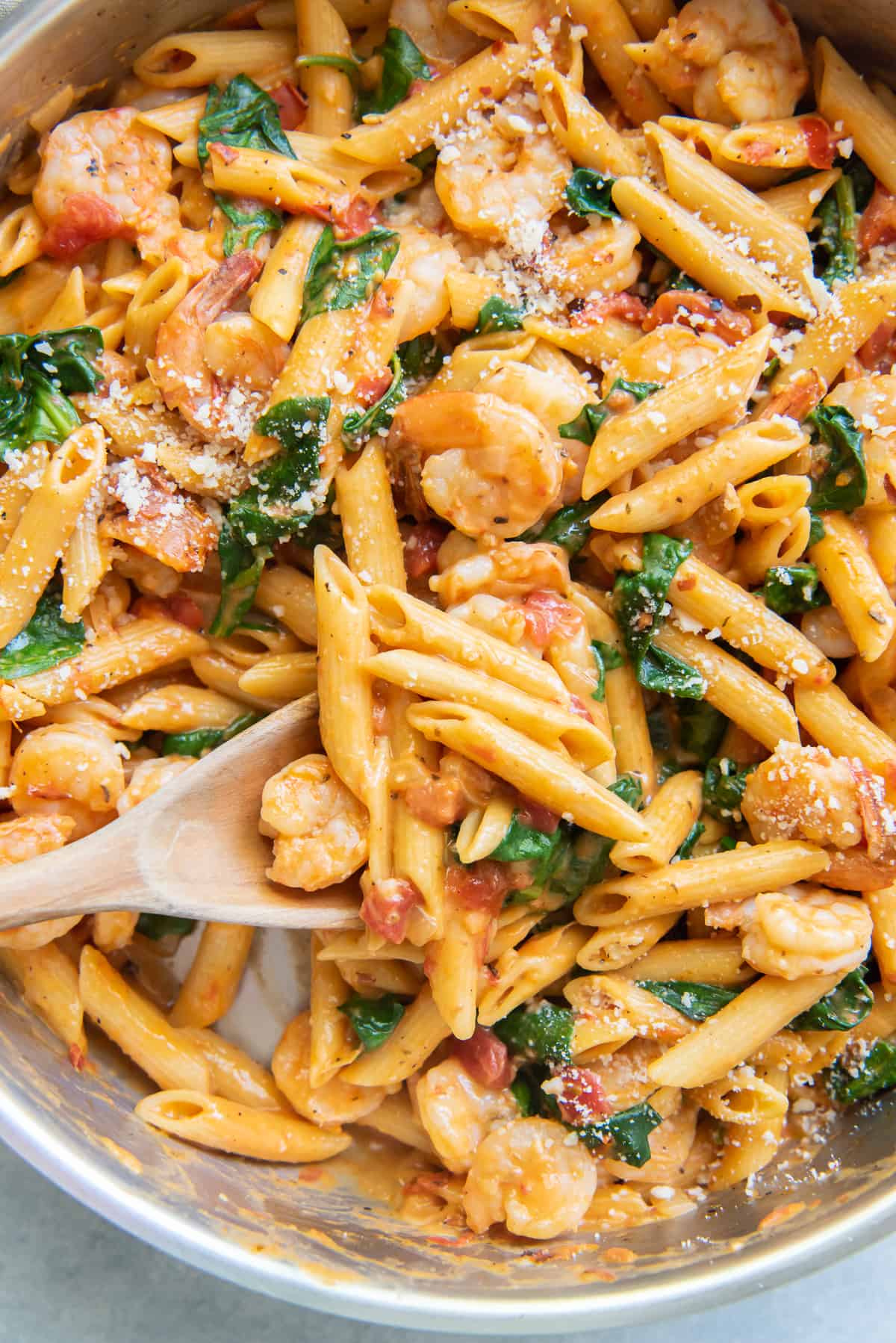 A spoon scoops pasta with shrimp and spinach from a skillet.