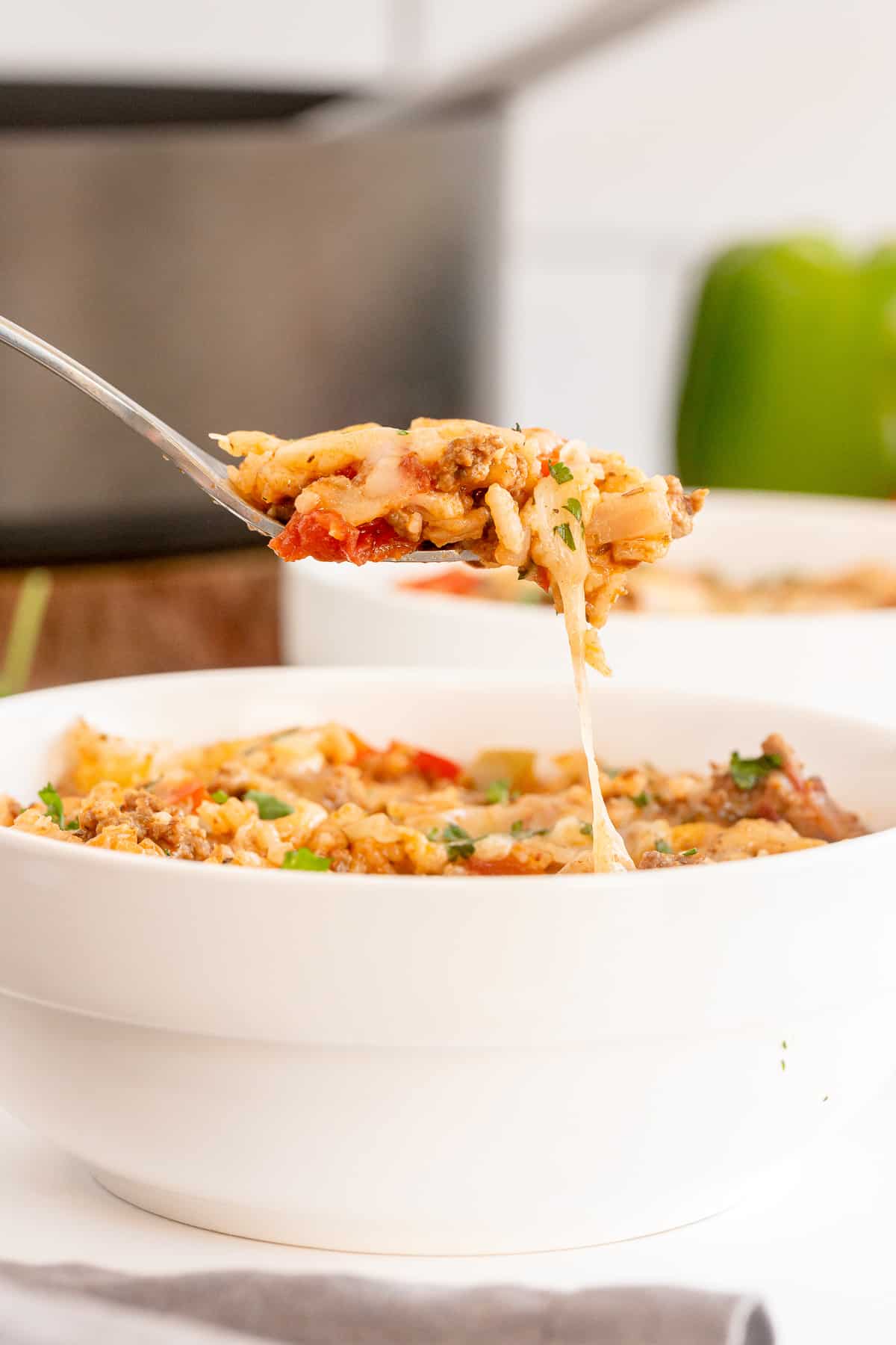 A fork lifts a stuffed pepper mixture from a white bowl.