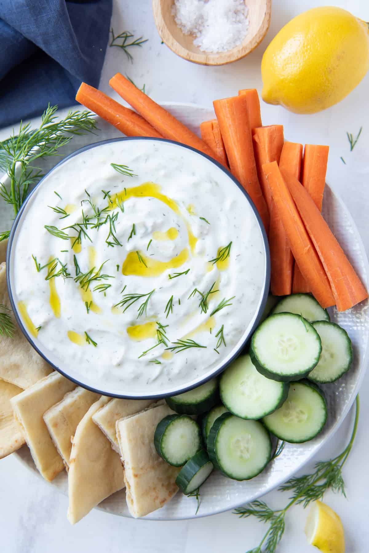 An over the top shot of a bowl of Tzatziki on a platter with veggies and pita.