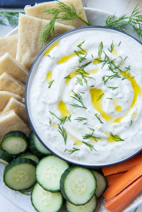 A bowl of Tzatziki on a plate with veggies and pita shot from over the top.