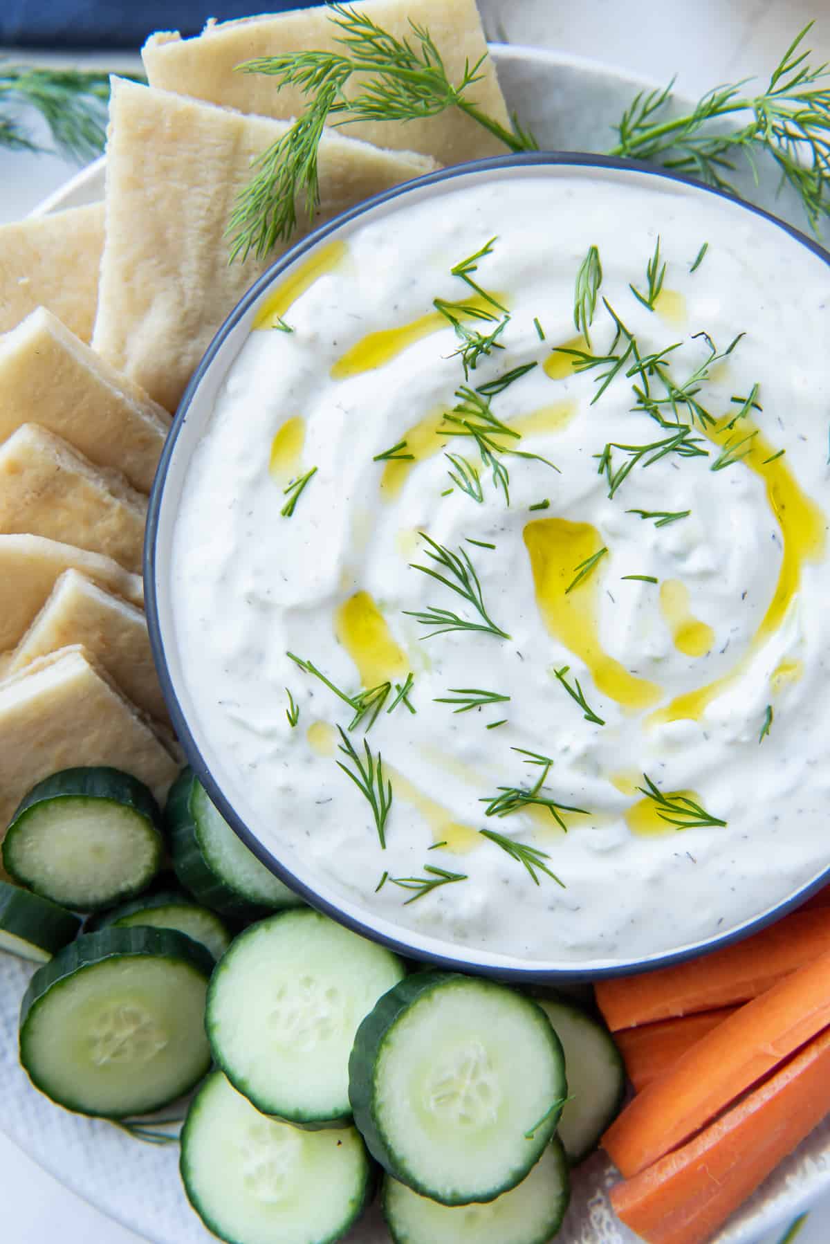A bowl of Tzatziki on a plate with veggies and pita shot from over the top.