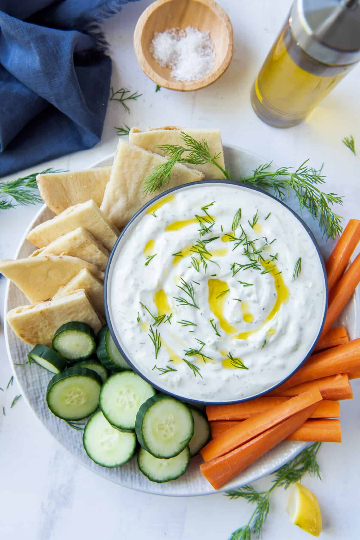A bowl of Tzatziki on a plate with veggies and pita.