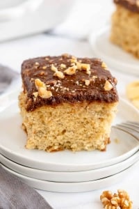 A closeup of a slice of Banana Cake with Chocolate Walnut Glaze on a white plate.