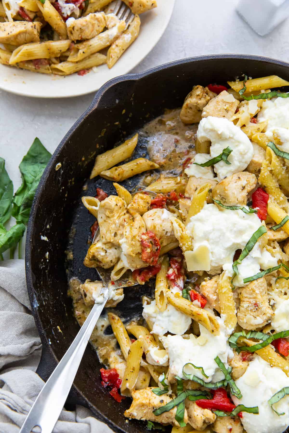 A serving spoon rests in a skillet full of Chicken Pesto Pasta.