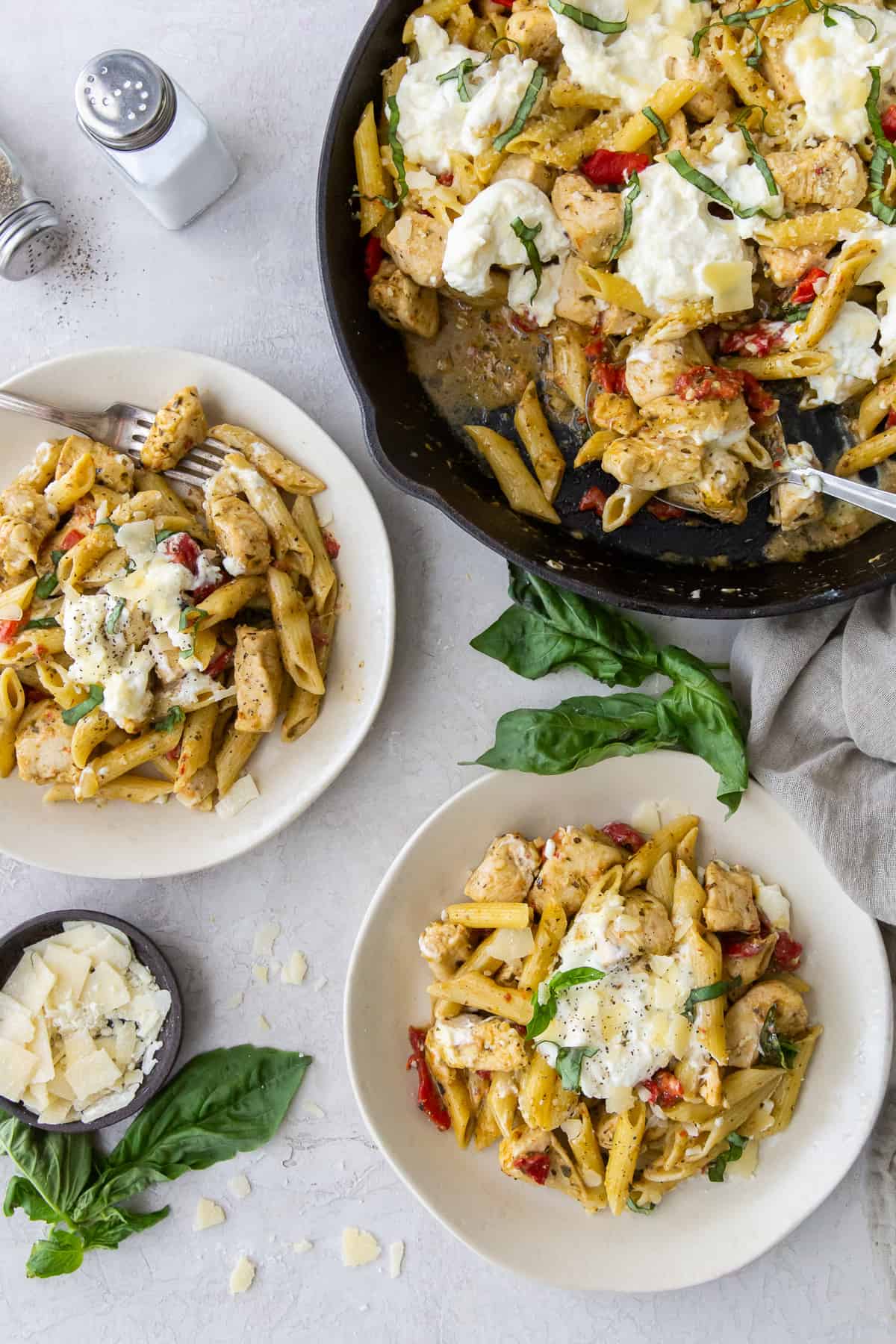 Two bowls of Chicken Pesto Pasta next to a skillet.
