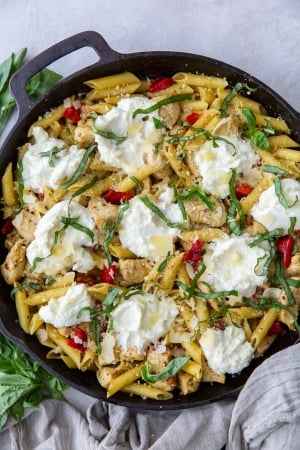 A cast iron skillet filled with pasta topped with scoops of ricotta cheese.